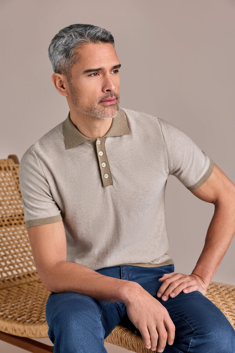Man draagt zandbeige polo met knopen en zit op een stoel.
