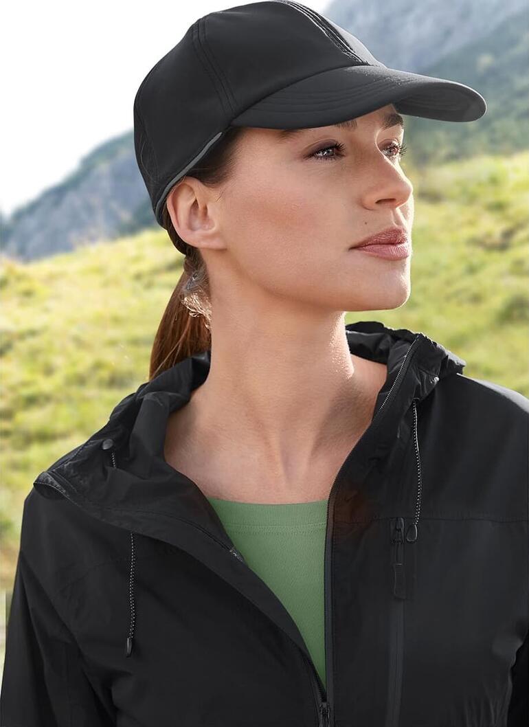 Softshell pet Vrouw met een zwarte softshell pet en jas in een natuurlijke omgeving.