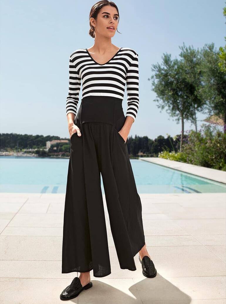 Elisa F. Ibiza-broekrok Vrouw in gestreepte tover-shirt met zwarte broek, staat voor het zwembad.