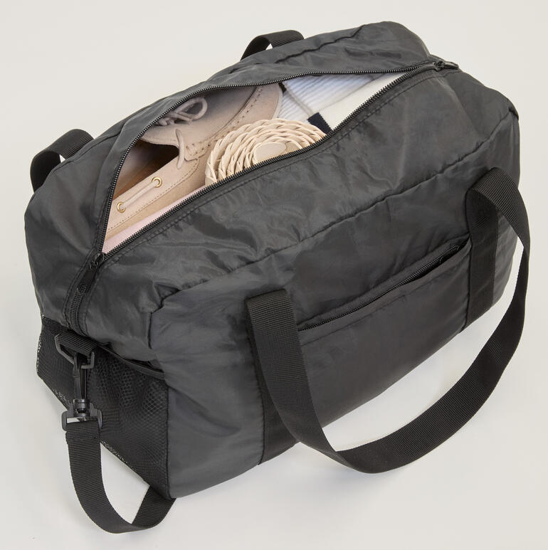 Opengevouwen opvouwbare reistas met schoenen en andere spullen.