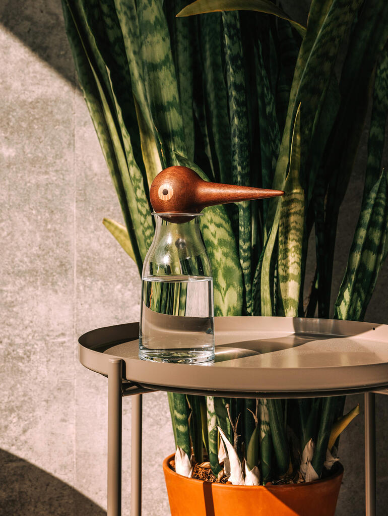 Glas water met houten vogelvormige waterdispenser op een tafel.