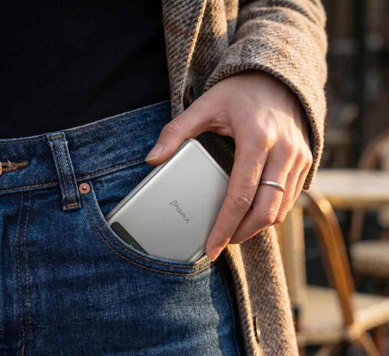 Een hand steekt een zilveren powerbank in een broekzak.