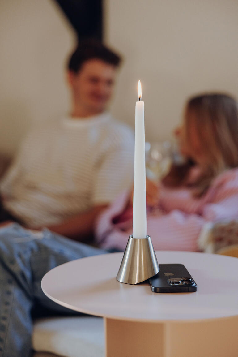 Kaars in metalen houder op tafel, achtergrond met mensen.