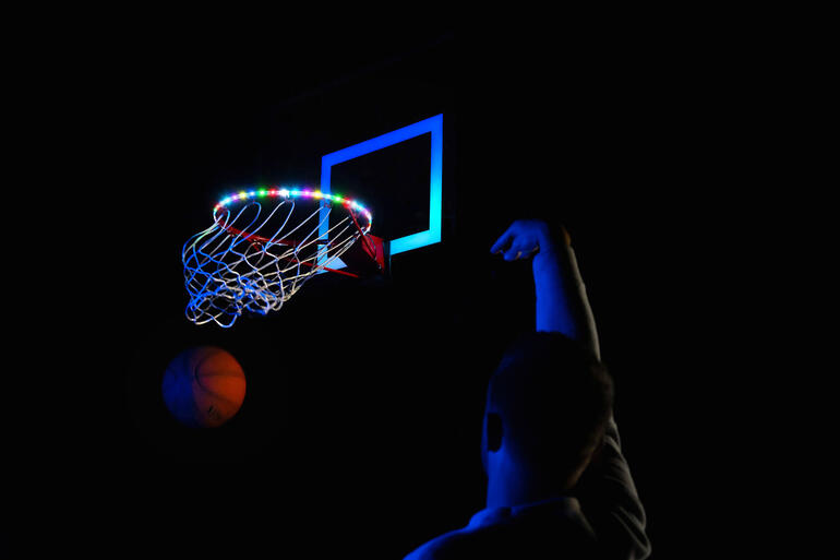 Basketbalnet met kleurrijke LED-lampen en persoon die gooit op een donkere plek.