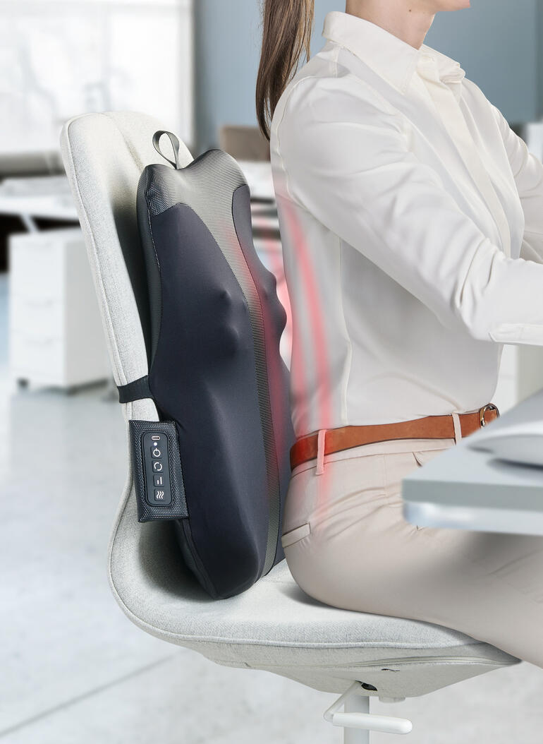 Rugmassageapparaat bevestigd aan een bureaustoel terwijl iemand werkt.