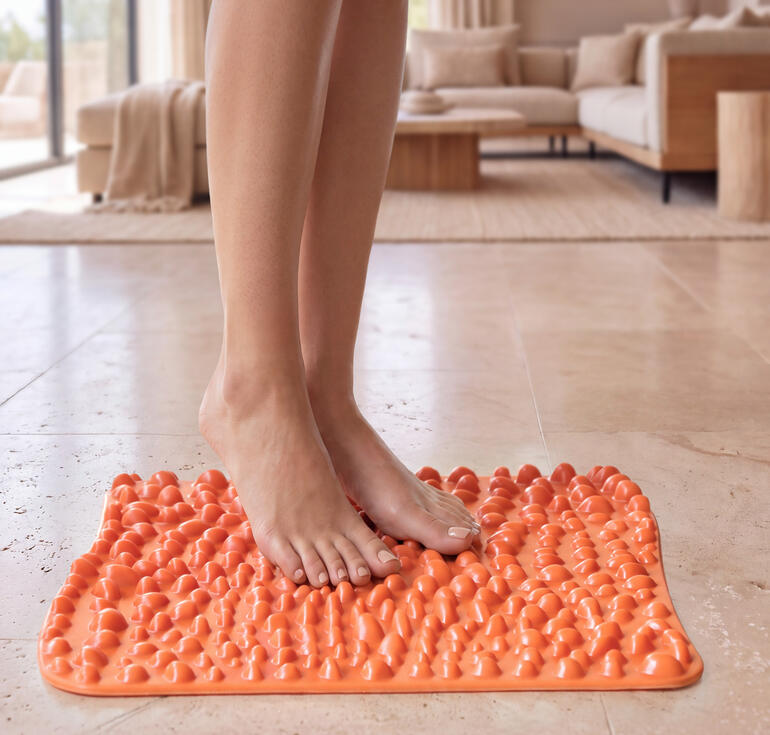 goFit voetreflexmat in feloranje, op een lichte vloer met voeten erop.