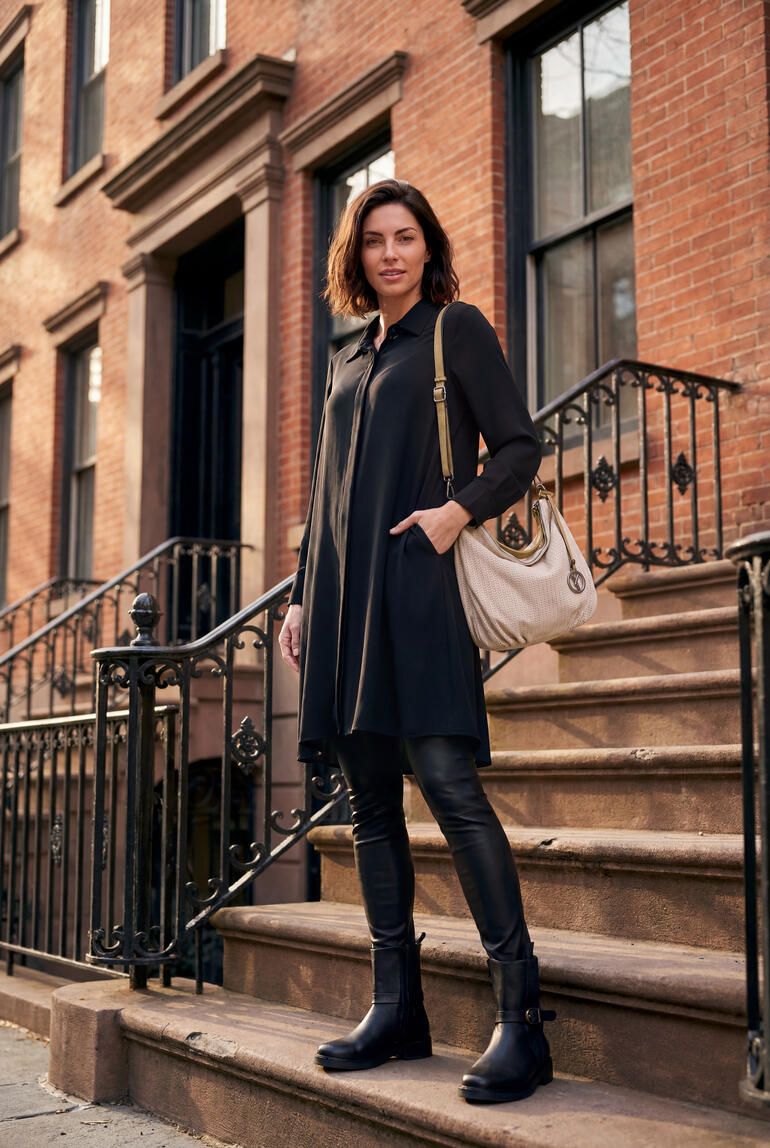 Vrouw in een lange blouse en leggings staat op de trap van een historisch gebouw.