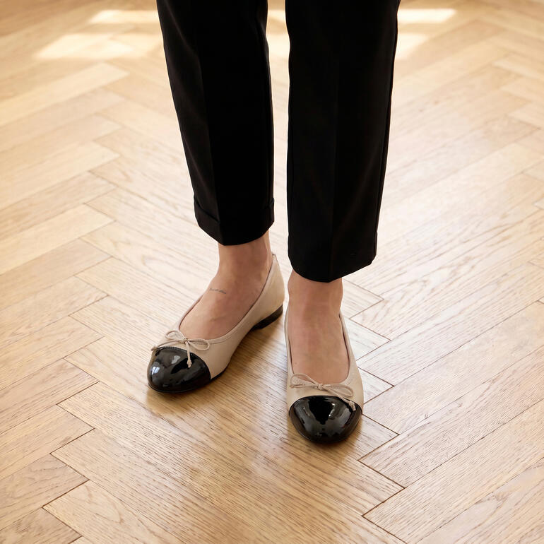 Beige ballerina's met een zwarte neus op een houten vloer