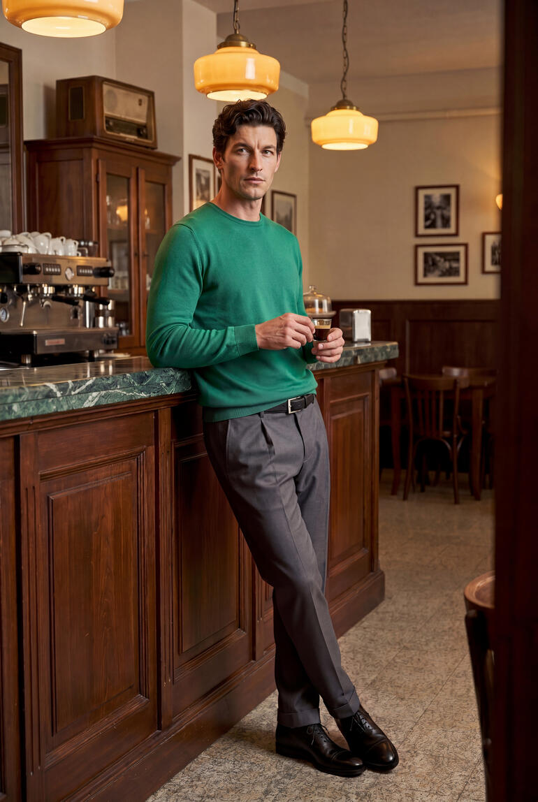 Man in Junghans 1954 zijde sweater leunt tegen de bar van een café.