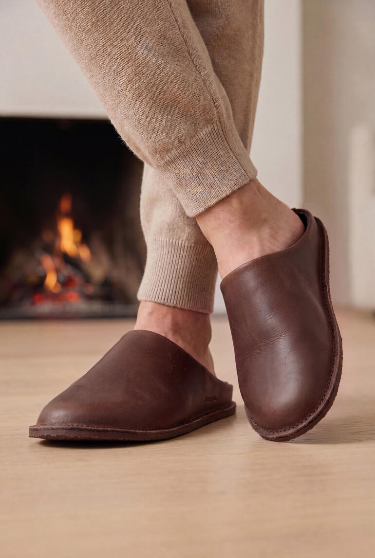 Bruine leren slippers aan de voeten van een persoon voor een open haard