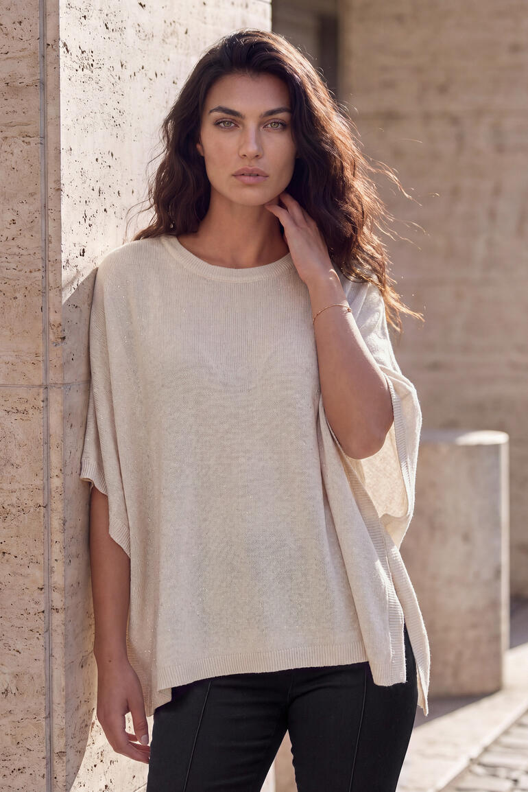 Vrouw in een beige kasjmier glamour poncho voor een muur