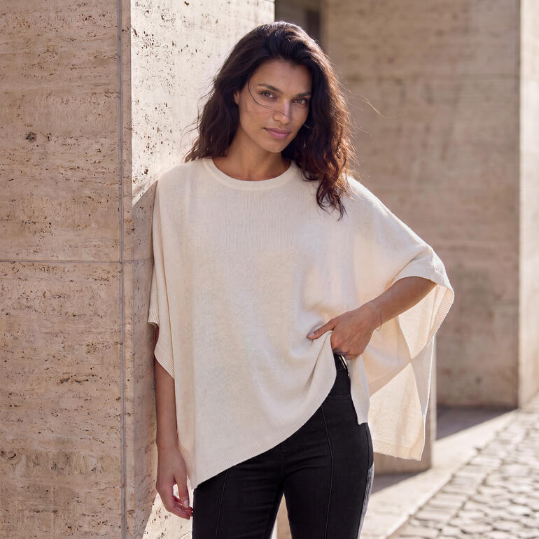 Vrouw draagt beige kasjmier glamour poncho tegen een muur