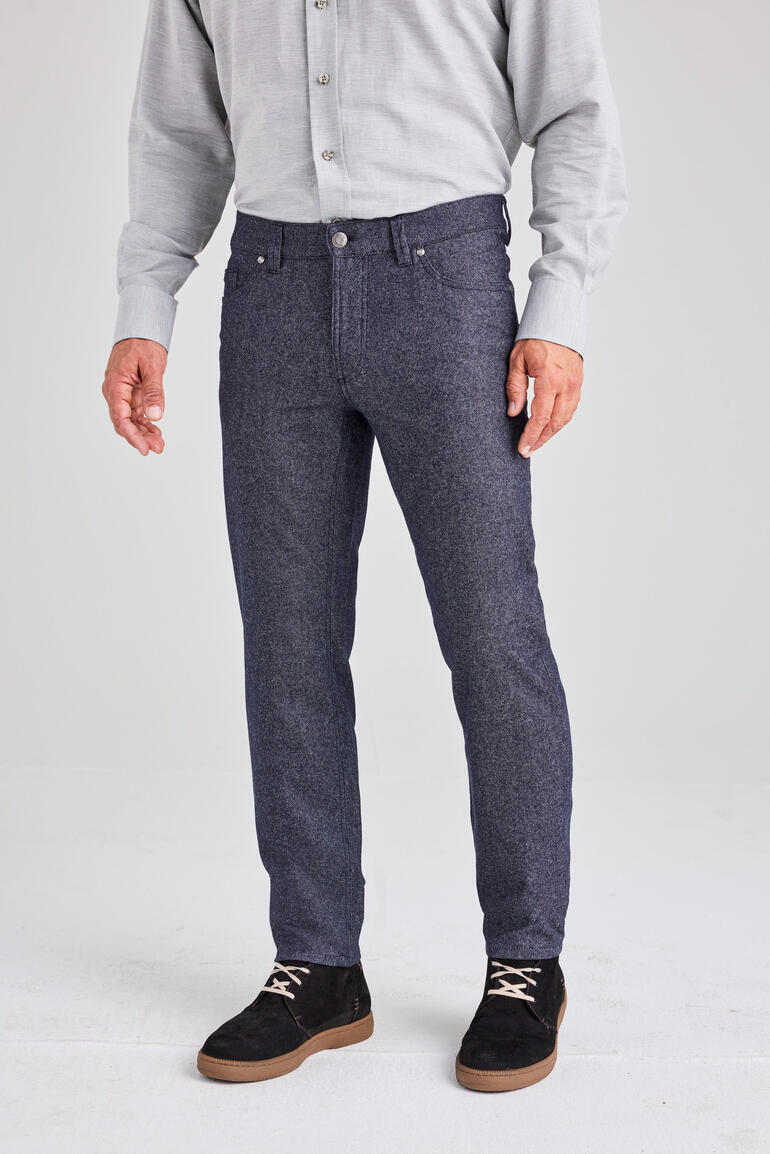 Man met een grijs overhemd en wollen jeans staat voor een lichte achtergrond