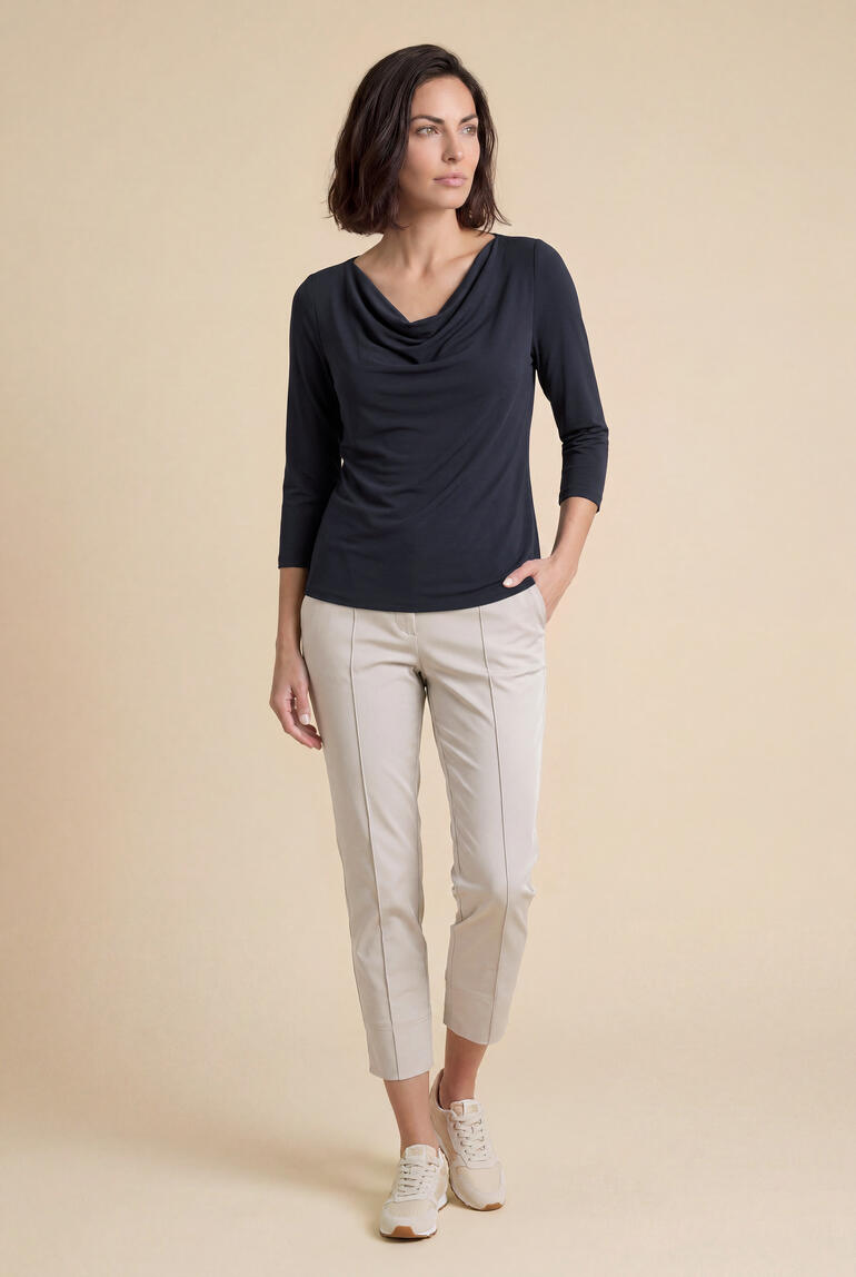Vrouw in Modal Micro-Waterfallkraag-shirt en lichte broek poseert voor een beige achtergrond