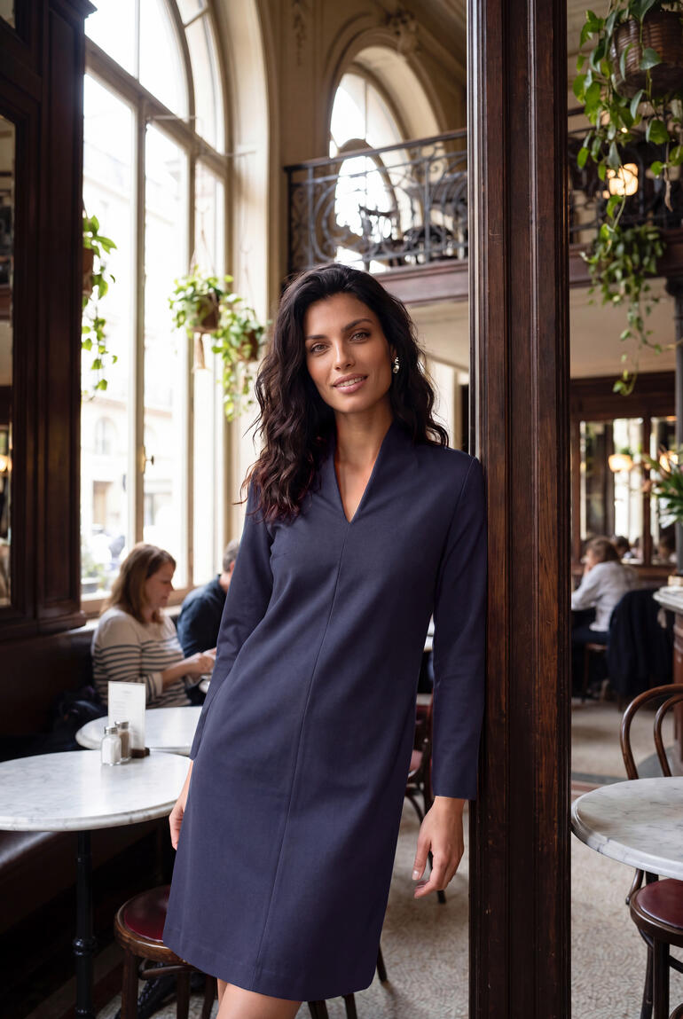 Vrouw in een klein blauwe kleed met kelk-kraag in een café.
