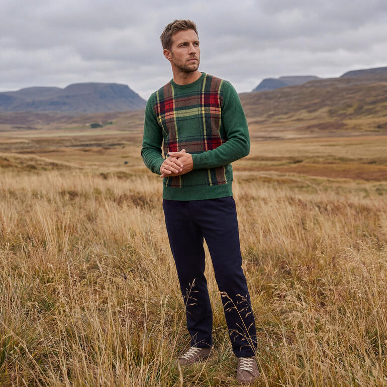 Man in groene tartan trui staat in een herfstlandschap.