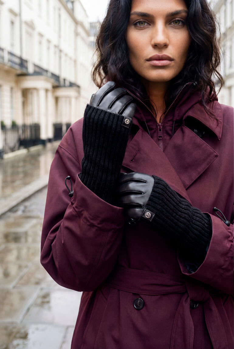 Vrouw in een paarse trenchcoat staat op een regenachtige straat.