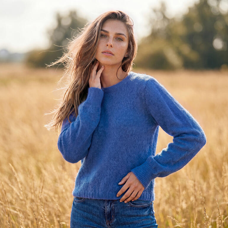 Vrouw in een blauwe alpaca-mohair trui staat op een veld.