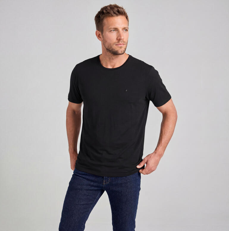 Man in zwart merinowollen shirt staat voor een neutrale achtergrond.