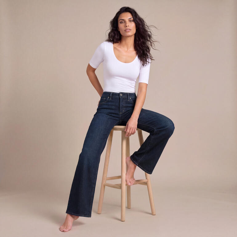 Vrouw in wit T-shirt en comfortabele jeans zit op een kruk