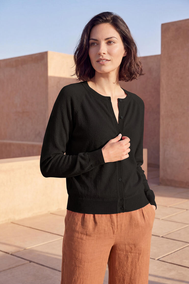 Vrouw in zwarte korte cardigan staat voor architectuur.