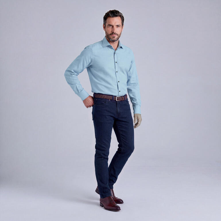 Man in overhemd en jeans, in zelfverzekerde pose.